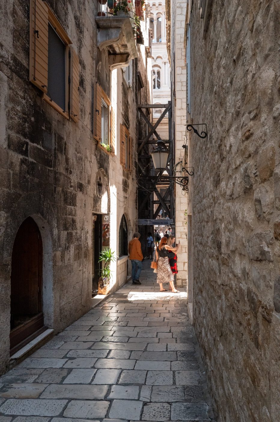 Silhouettes of passers-by in an alley with the bell tower in the background, Split