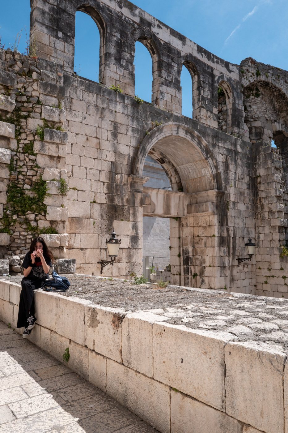 Young woman sitting on a low wall near the Roman arcades, Split
