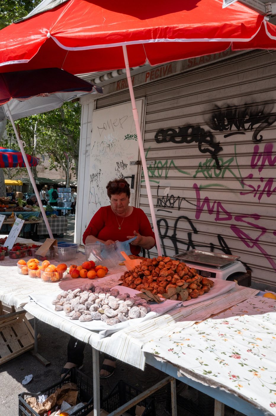 Street vendor preparing doughnuts and apricots under a red parasol, Split