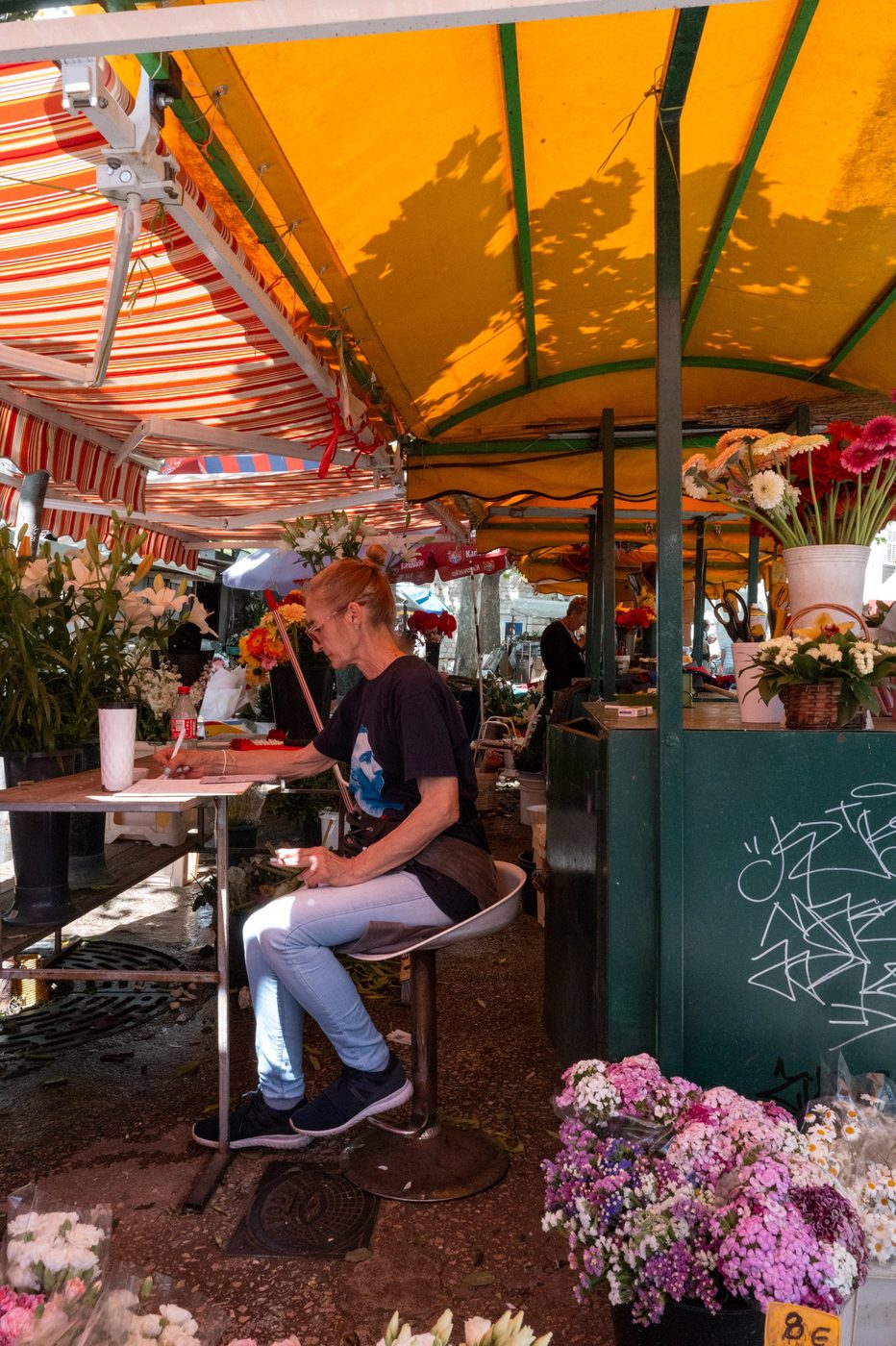 Florist sitting and writing labels under an orange tarpaulin, Split