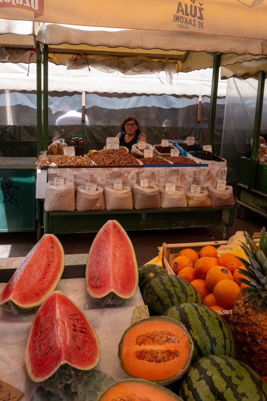 Market vendor surrounded by dried fruit, watermelons and oranges, Split