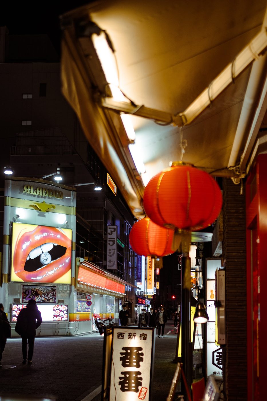 Four employees in suits and masks crossing in front of a lit fish shop, Tokyo