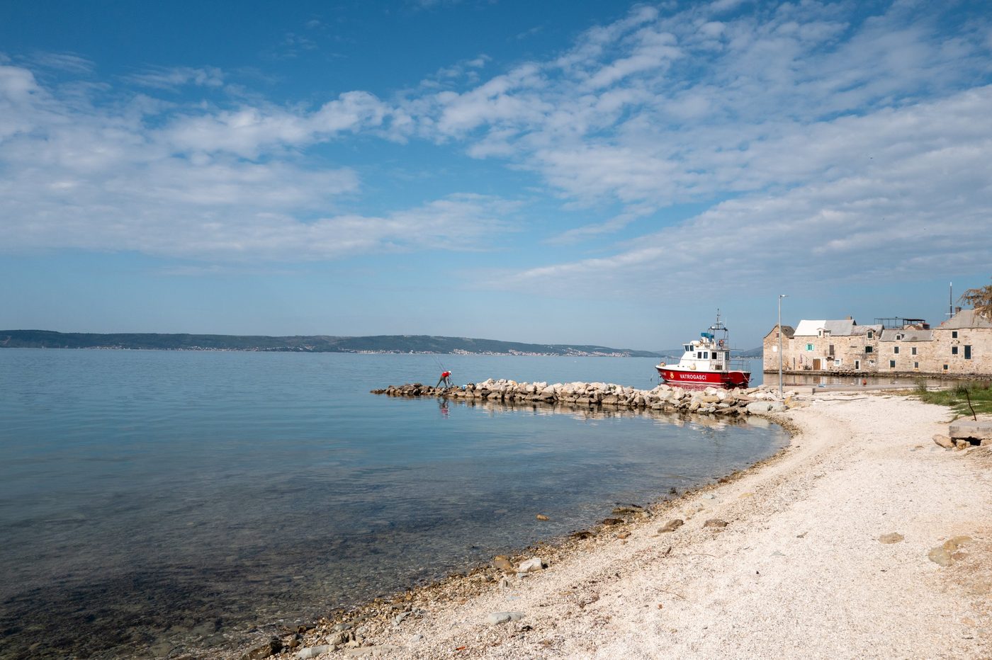 Fisherman on a stone jetty near a red fire boat, Trogir