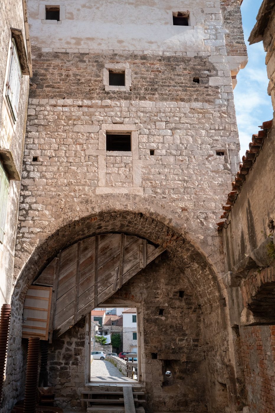 Old wooden gate beneath a stone arch in an alleyway, Trogir