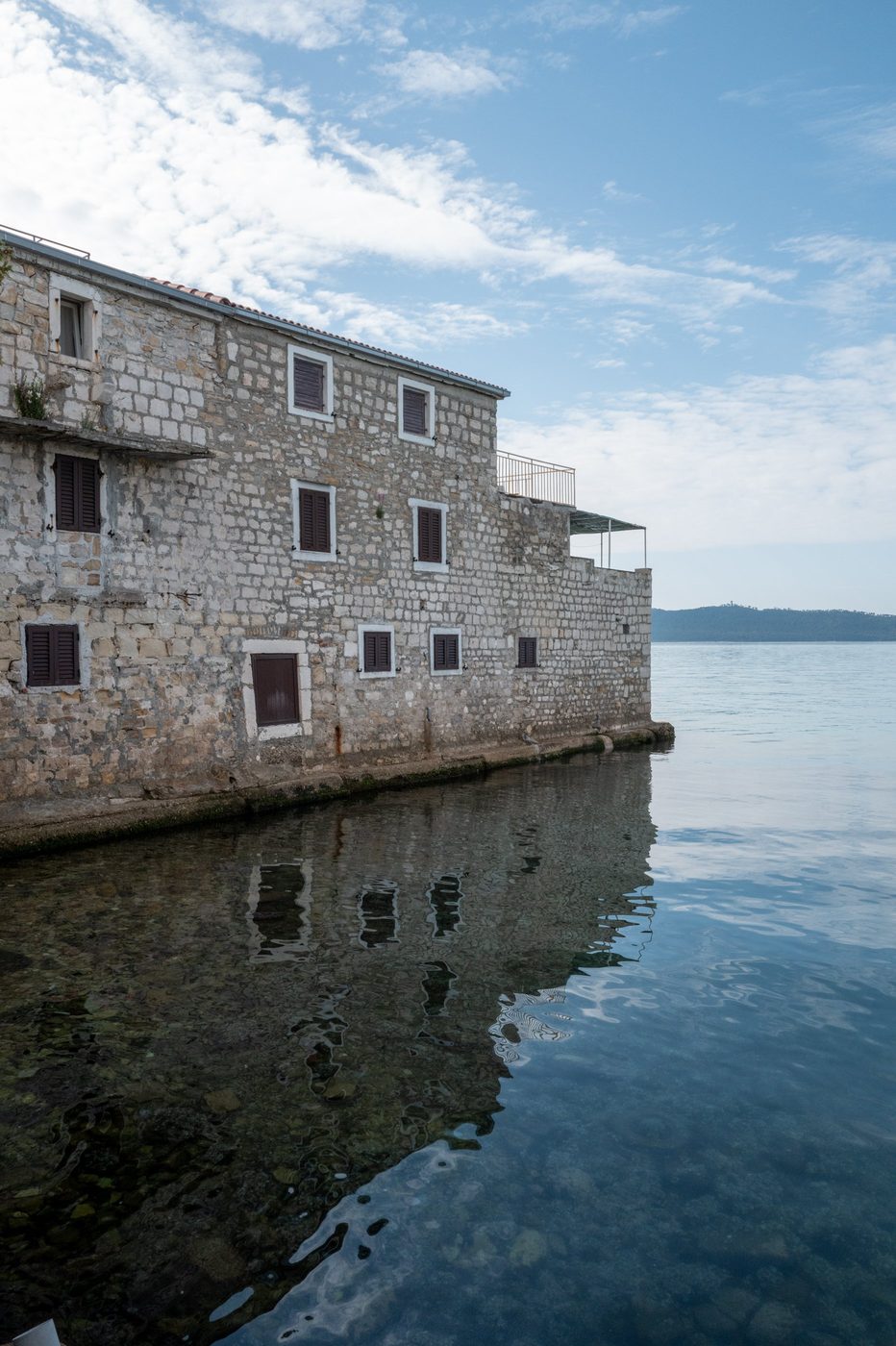 Stone façade with colorful shutters reflected in the sea, Trogir