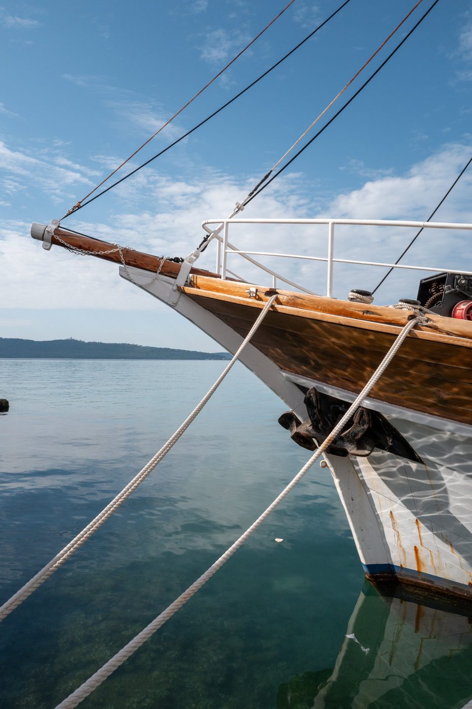 Bow of a moored wooden sailboat, ropes stretched over the calm water, Trogir