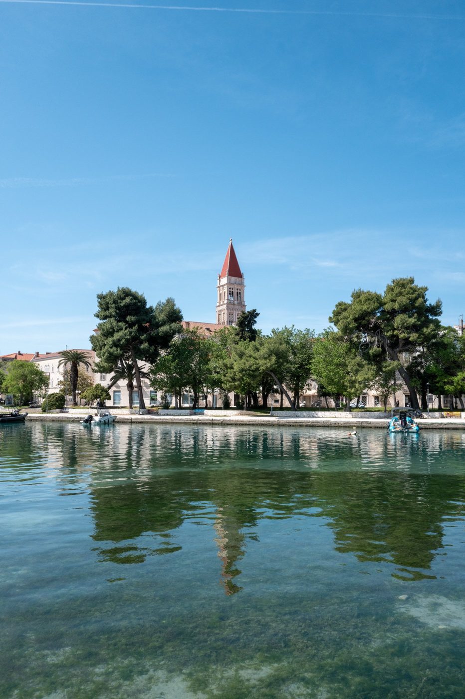 Cathedral bell tower rising above the pines, reflected in the canal, Trogir