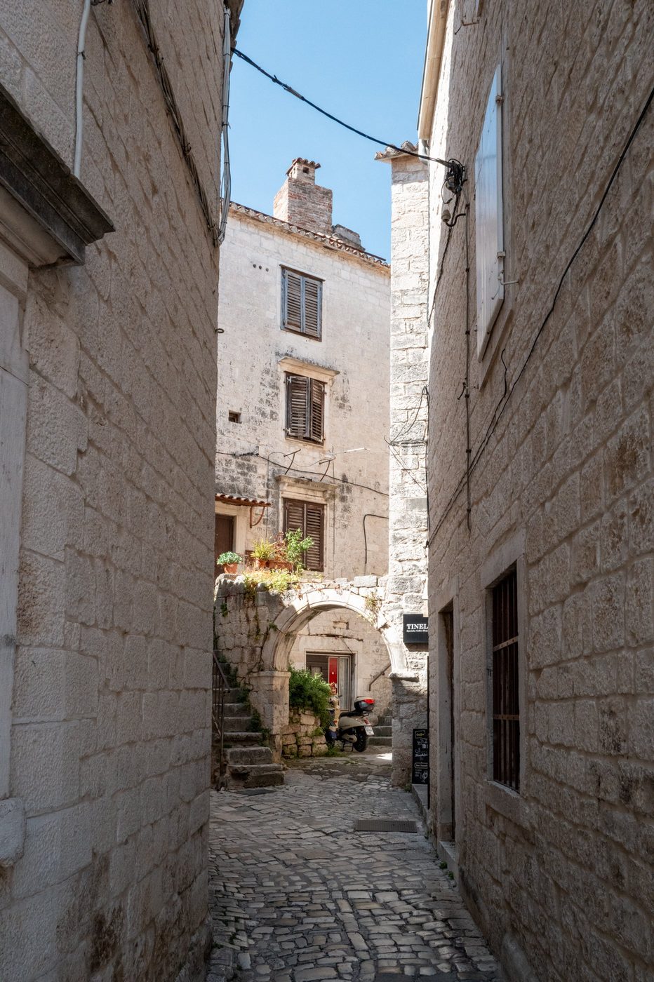 Narrow alley leading to a vaulted porch with a parked scooter, Trogir