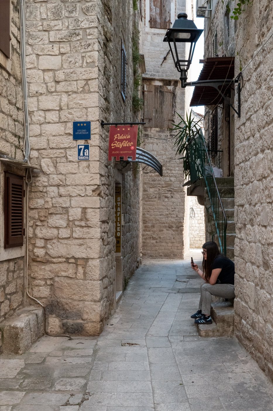 A passerby sitting on a doorstep, absorbed in her phone, Trogir
