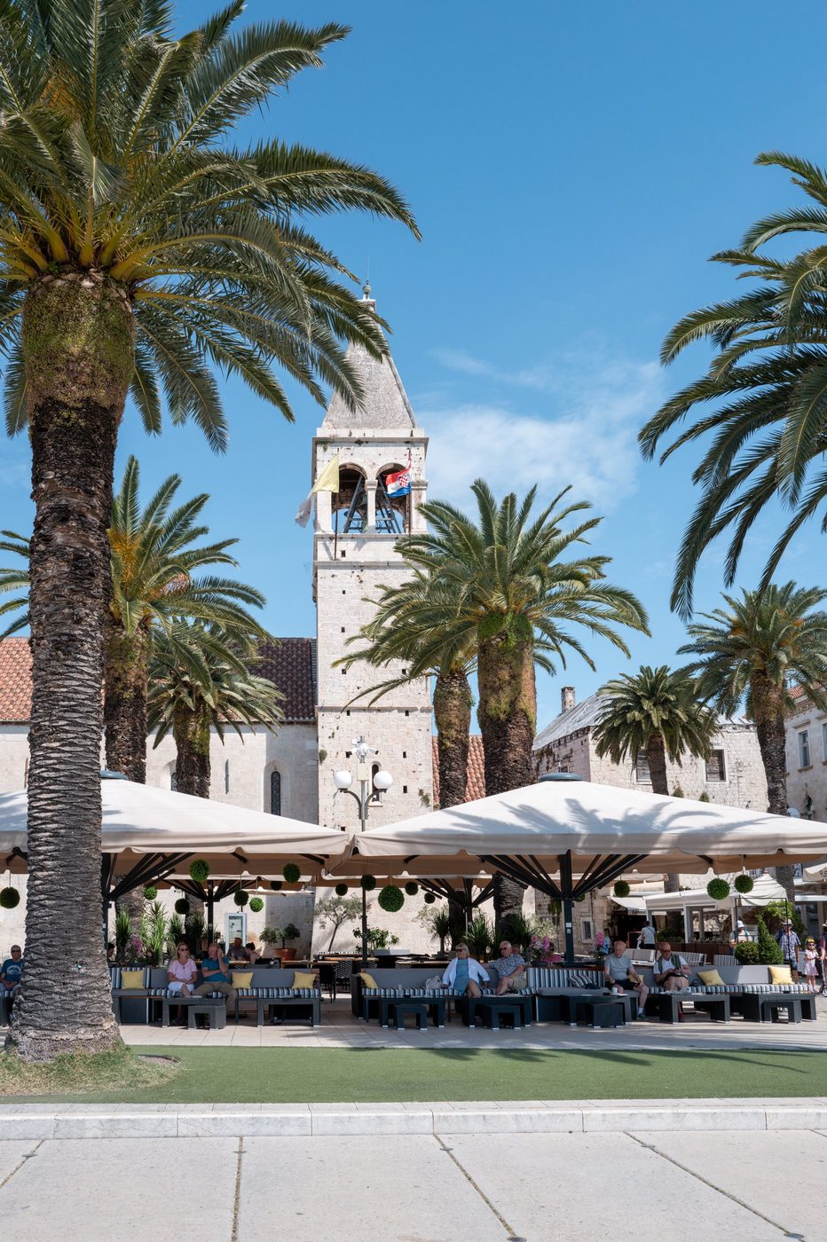 Shaded terrace beneath the bell tower surrounded by palm trees, Trogir