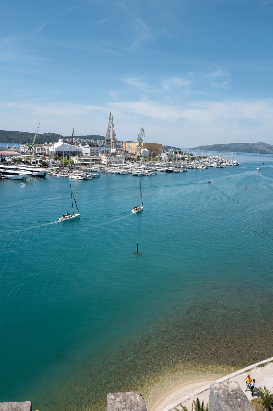 Two racing sailboats leaving the harbor beneath the shipyard cranes, Trogir
