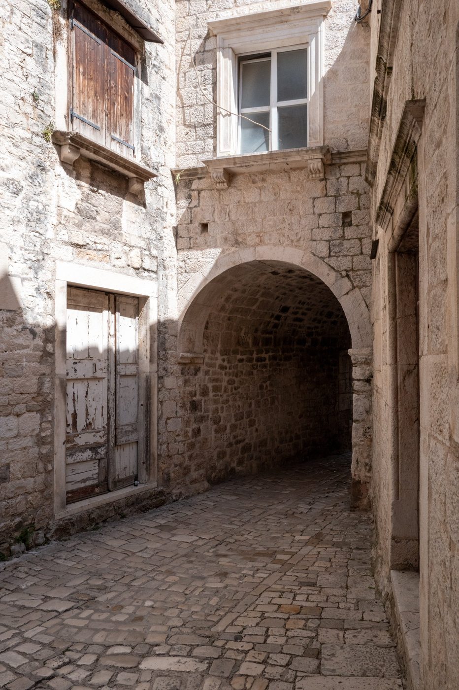 Vaulted passage between two old doors in a cobbled alley, Trogir