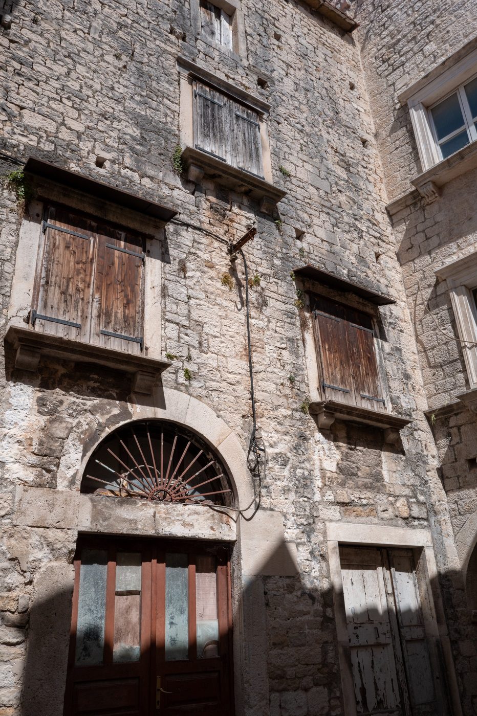 Worn façade with wooden shutters and a tired glass door, Trogir