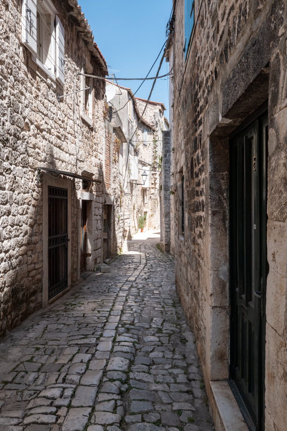 Quiet cobbled alley between light stone façades, Trogir