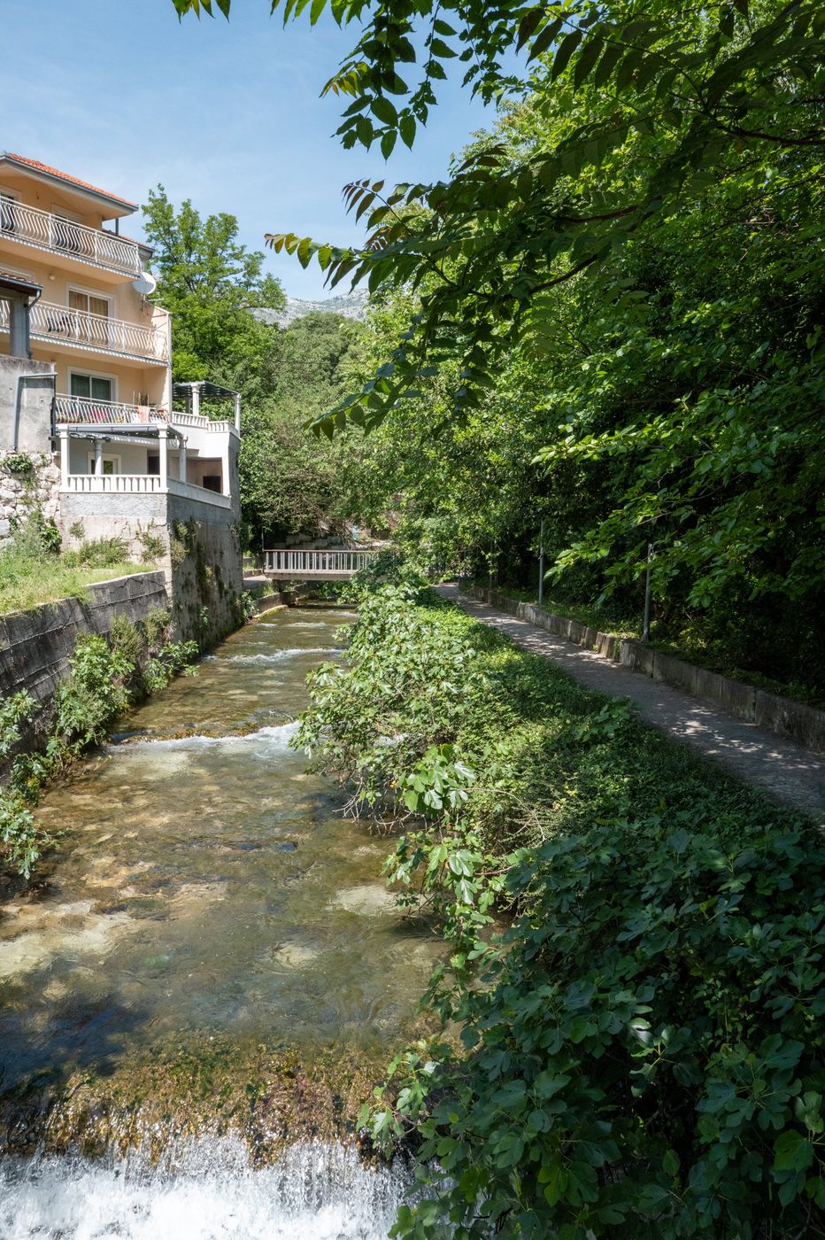 Small canal lined with greenery at the foot of a house with balconies, Trogir