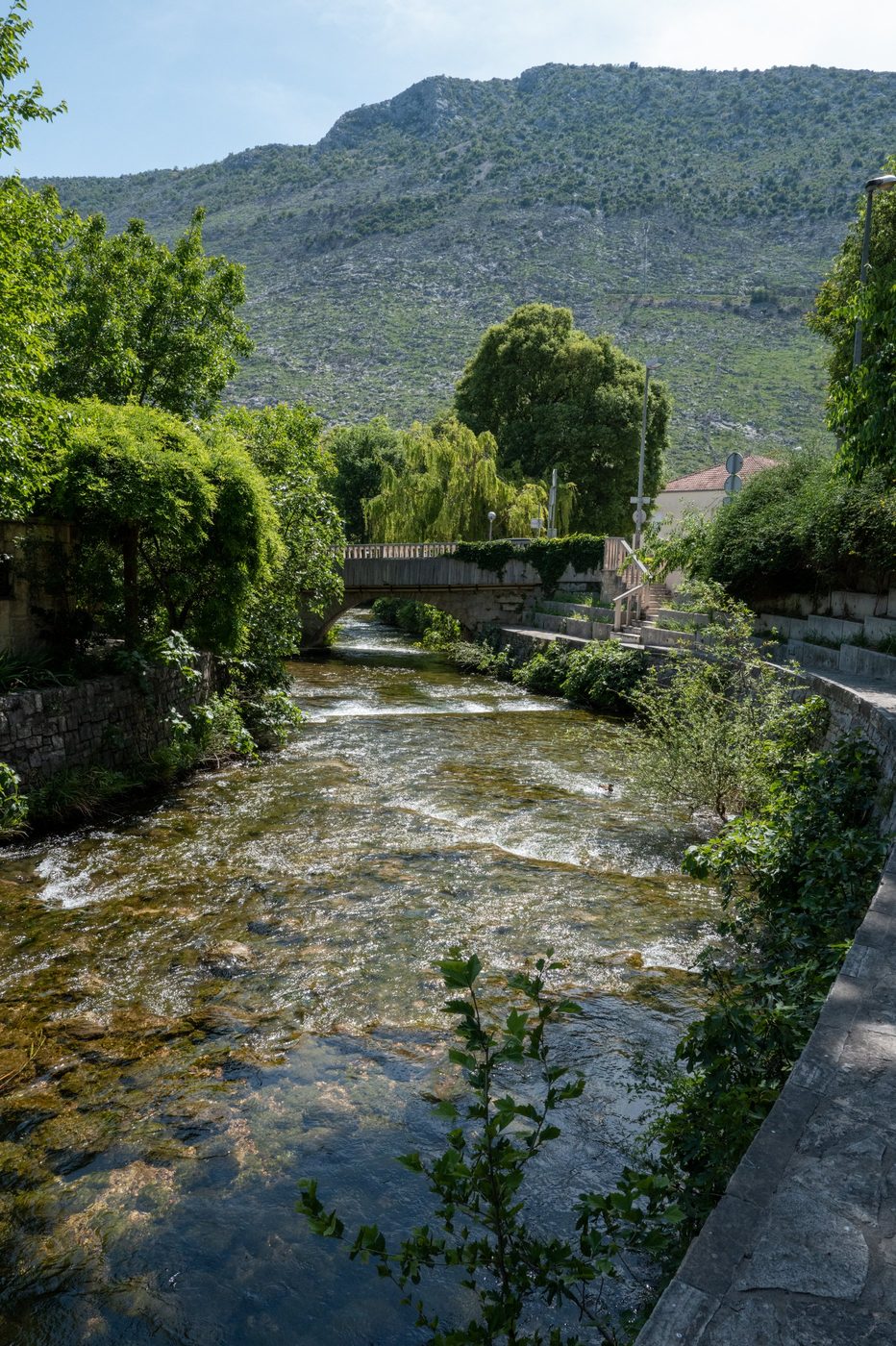 Bubbling river beneath a stone bridge, hill in the background, Trogir