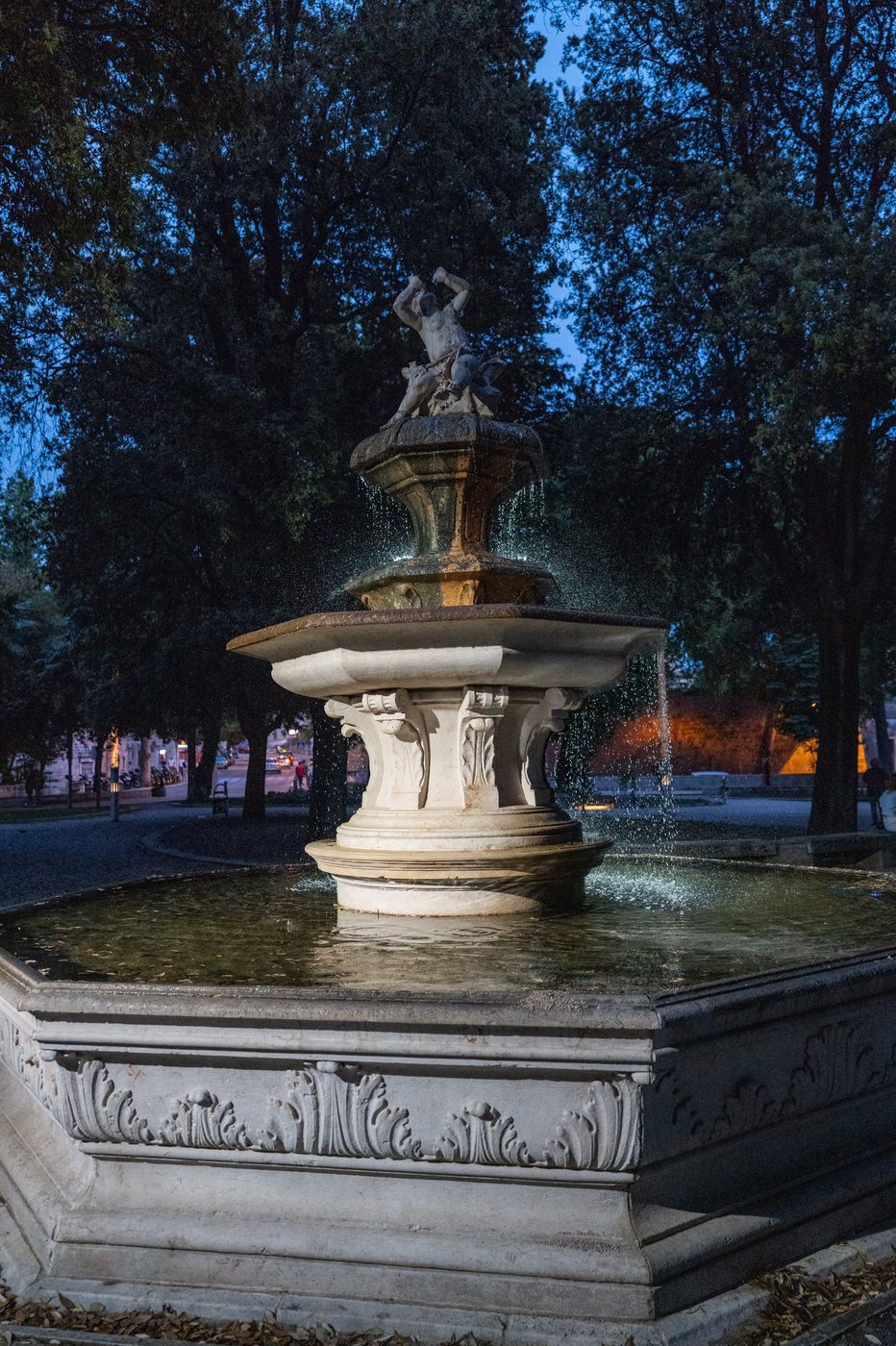 Fountain illuminated at night beneath the park's foliage, Trogir