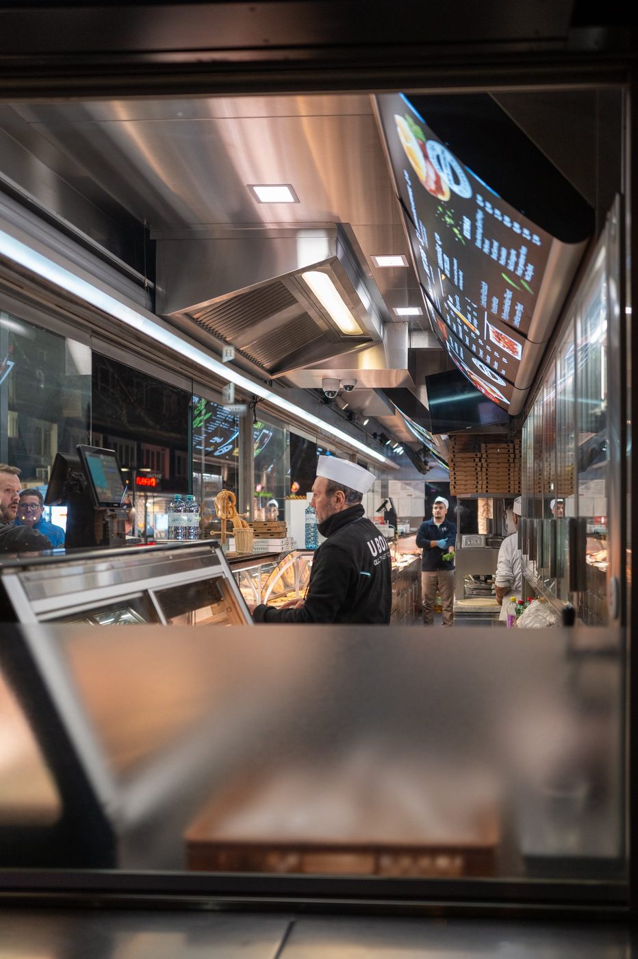 Chef in a toque serving under the illuminated menu of a snack bar, Vienna