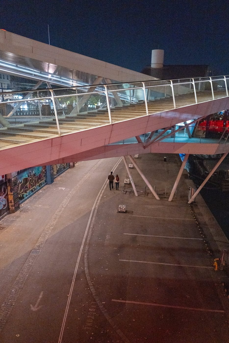 Couple walking under a metal footbridge lit up at night, Vienna