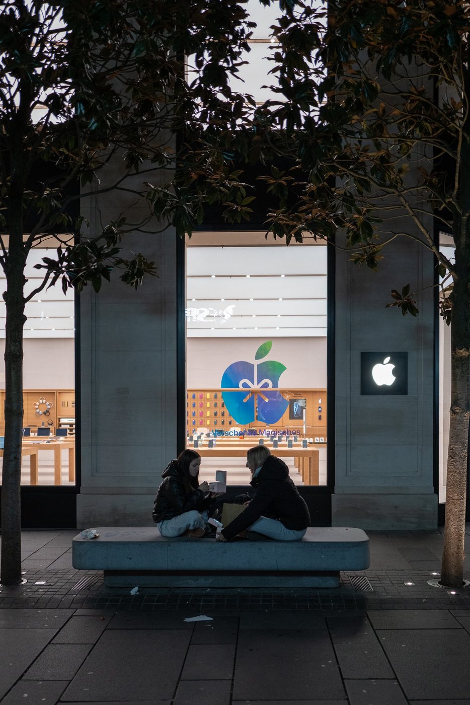 Two friends sitting on a bench in front of the Apple store window, Vienna