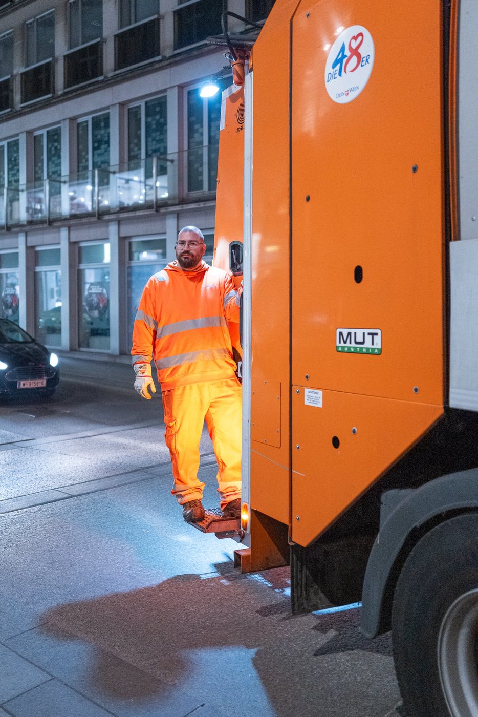 Garbage collector in hi-vis gear on the step of the collection truck, Vienna