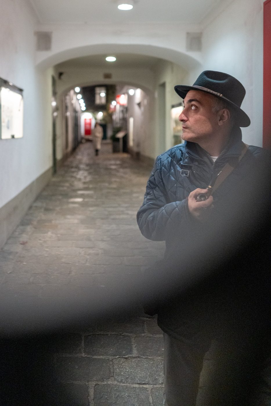 Man in a hat looking at a lit vaulted alley, Vienna