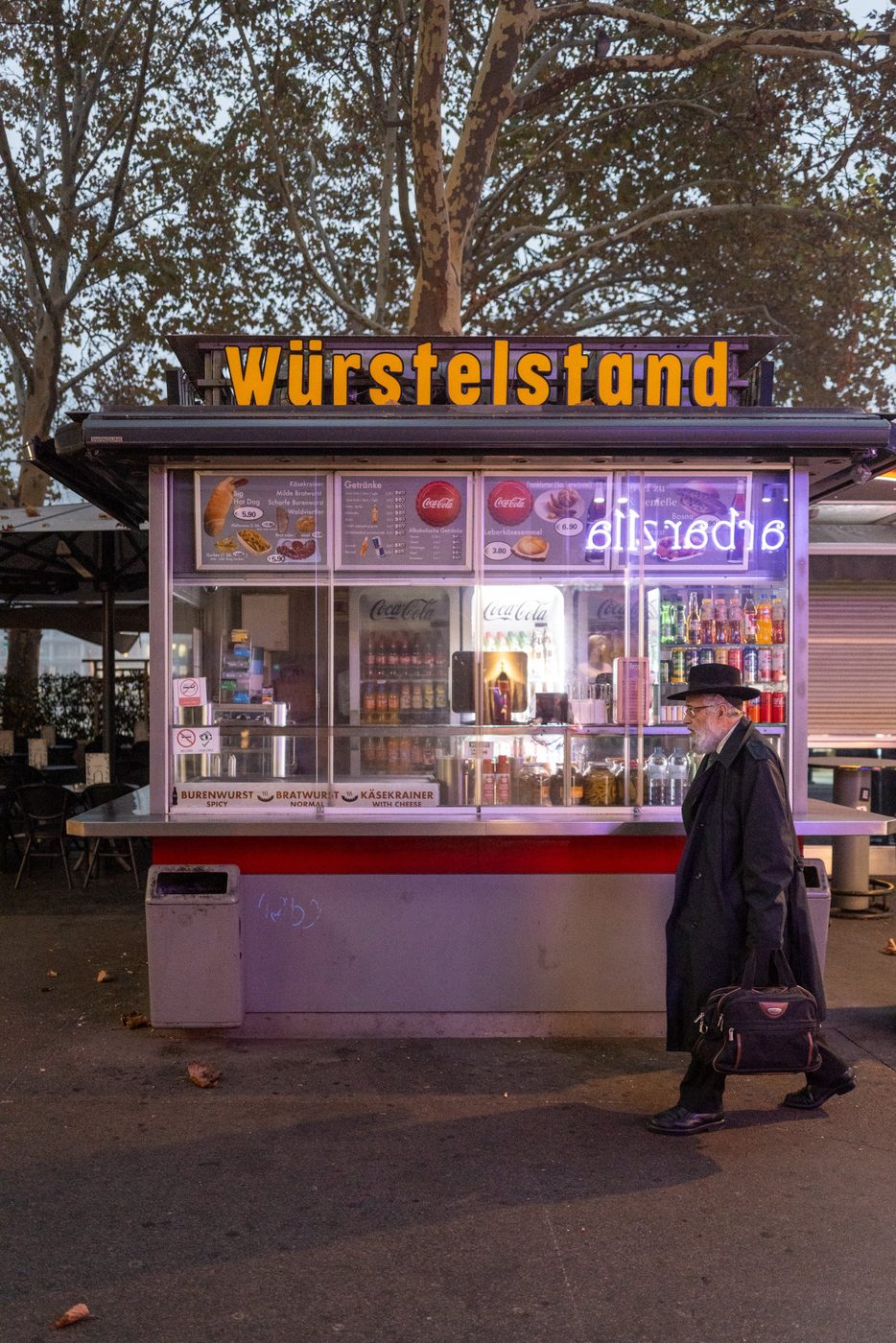 Man in a hat passing the illuminated Wurstelstand kiosk, Vienna