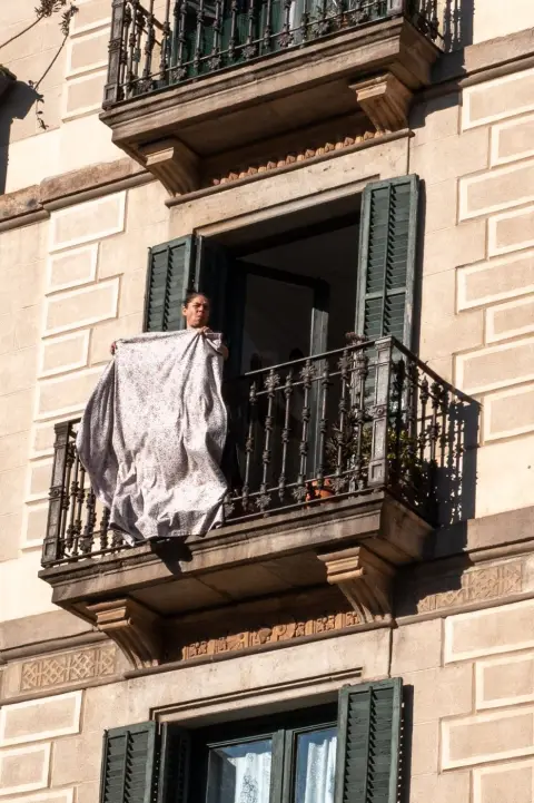Femme secouant un drap fleuri à un balcon en fer forgé, Barcelone