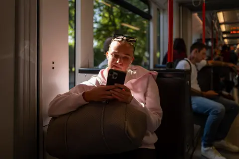 A young woman reading her phone on the tram, a bag on her lap, Bergen