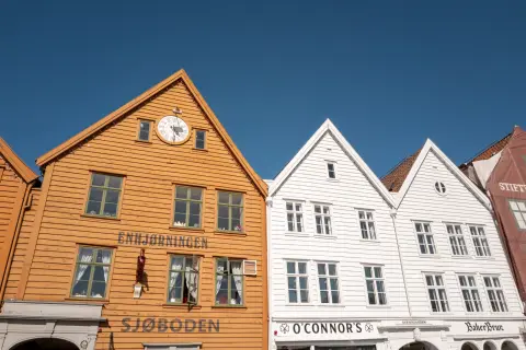 The orange and white wooden facades of Bryggen under a blue sky, Bergen
