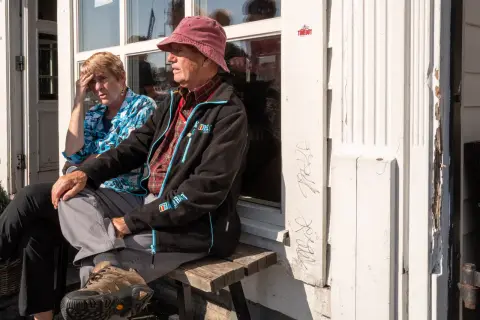 An elderly couple sitting in the sun on a bench, in front of a white door, Bergen