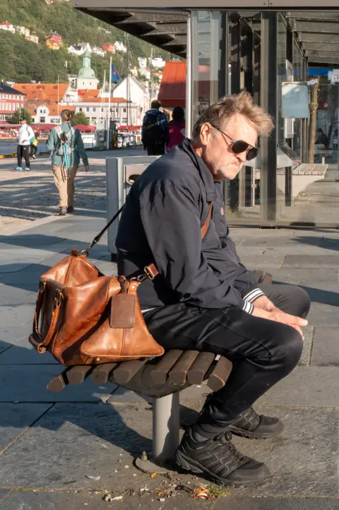 A man with a leather bag sitting on a bench, wearing dark glasses, Bergen