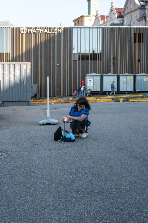A woman crouching in front of the Mathallen food hall, Bergen