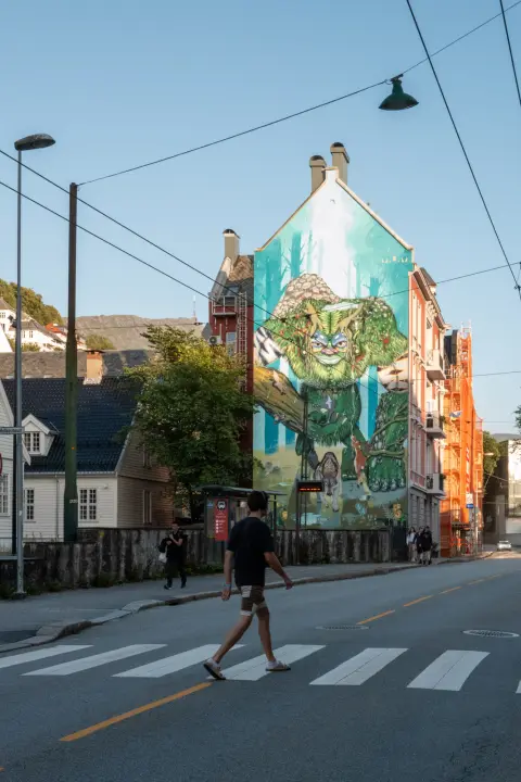 A passer-by crossing in front of a large green mural, Bergen