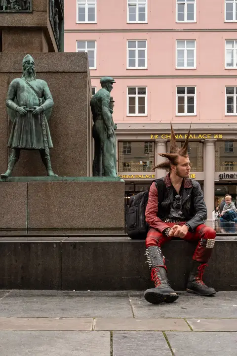 A punk with a red mohawk sitting at the foot of a bronze monument, Bergen