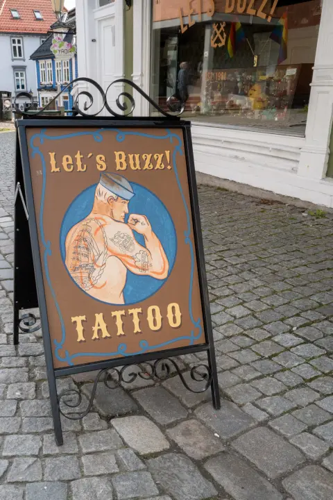 A “Let’s Buzz!” tattoo parlour sign on the cobbles, Bergen