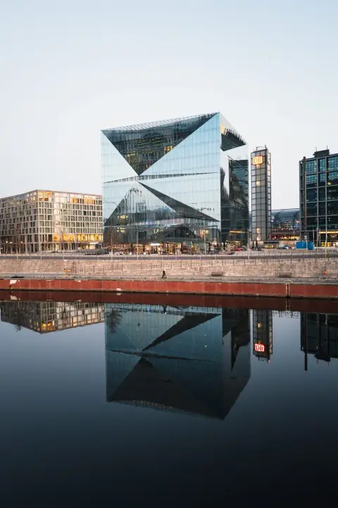 Immeuble de verre cubique et son reflet dans le canal, un passant longe le quai, Berlin