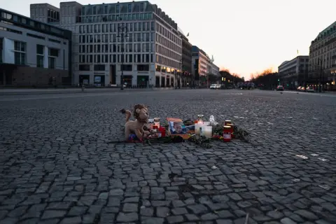 Bougies, fleurs et peluche déposées sur les pavés d'une place, Berlin