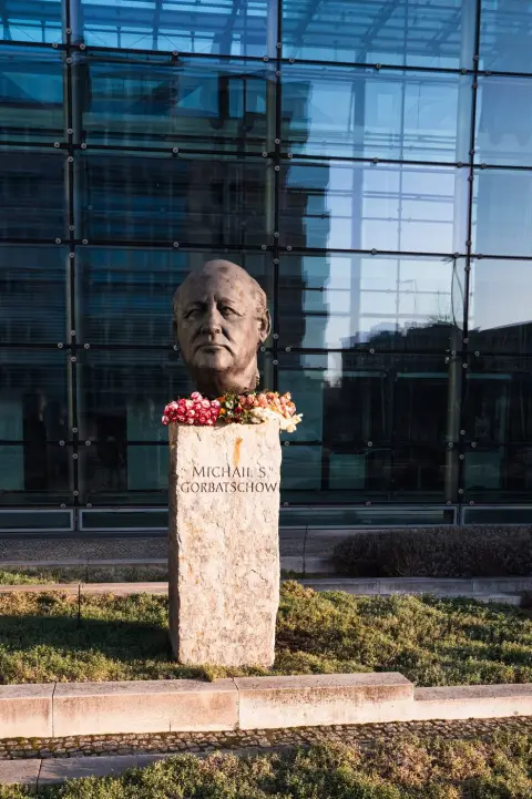 Buste en bronze fleuri d'un ancien dirigeant devant une façade de verre, Berlin