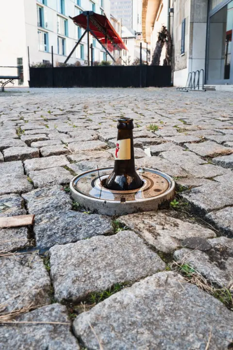 Bouteille de bière coincée dans une plaque d'égout entre les pavés, Berlin