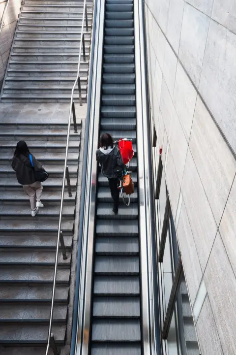Vue plongeante sur un escalator, une passante pousse un vélo à sacoche rouge, Berlin