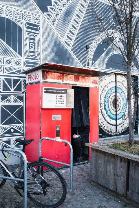 Cabine de photomaton rouge devant une fresque murale géométrique, Berlin