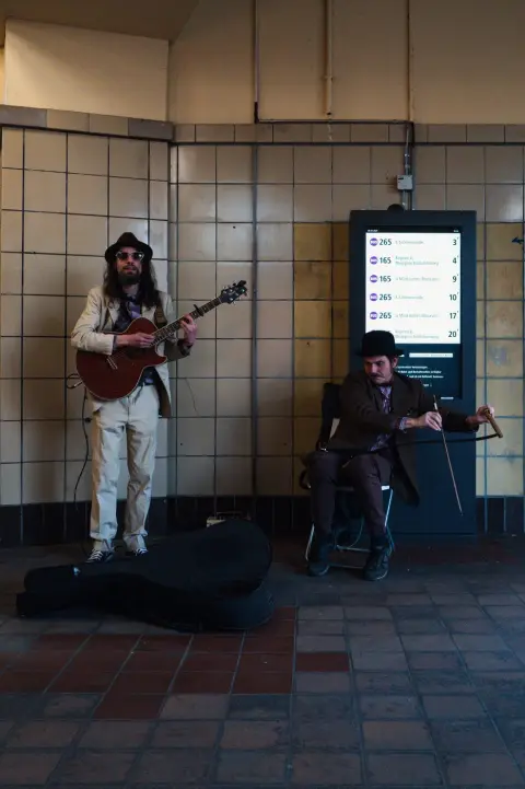 Duo de musiciens de rue jouant guitare et scie musicale dans un couloir carrelé, Berlin