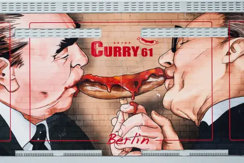 Fresque humoristique de deux hommes partageant une currywurst dégoulinante de sauce, Berlin