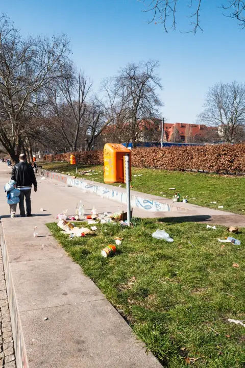 Père et enfant marchant le long d'une pelouse jonchée de détritus, Berlin