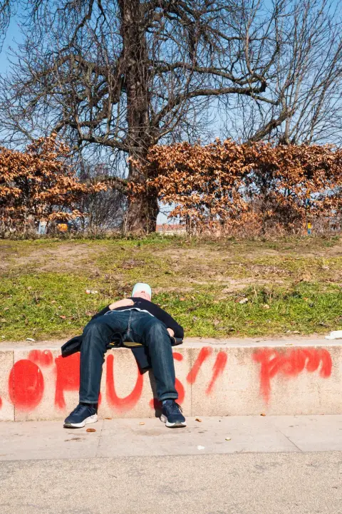 Homme allongé sur un muret taggé de rouge, sous un arbre dénudé, Berlin