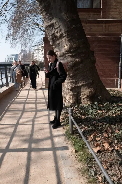Passante appuyée contre un arbre centenaire, ombres portées d'une grille, Berlin