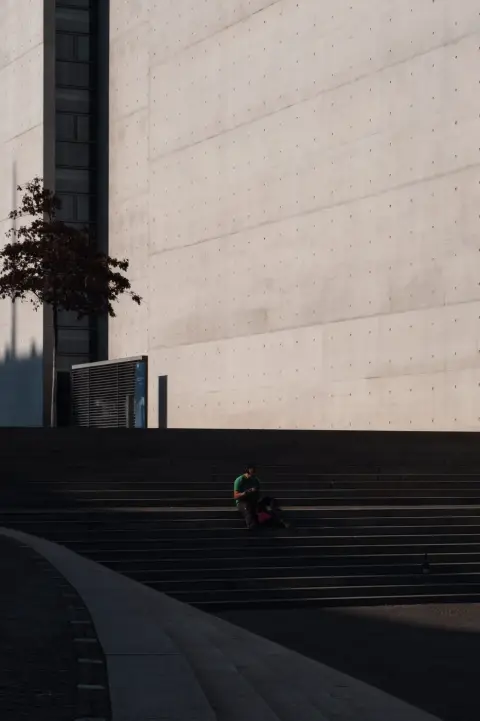 Homme assis seul sur de larges marches face à un mur de béton, Berlin