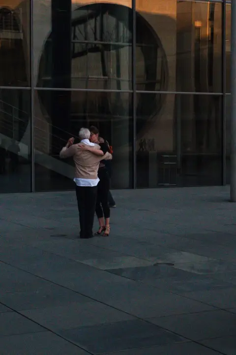 Couple âgé dansant enlacé devant une façade de verre au crépuscule, Berlin