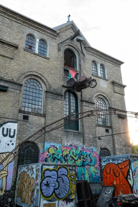 An old brick building covered in graffiti, a motorbike hung on the facade, Christiania, Copenhagen